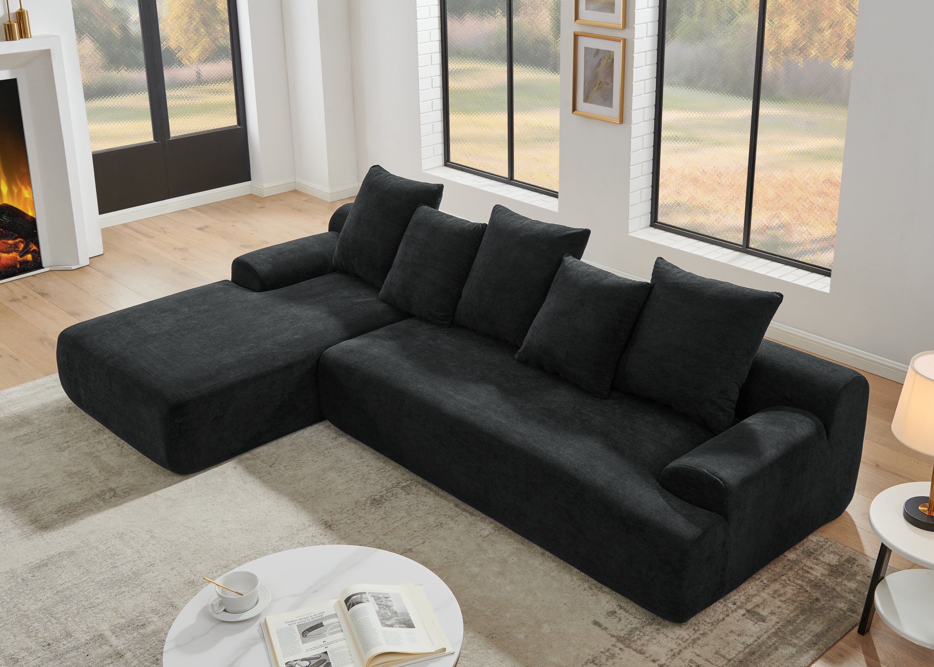 Contemporary black velvet modular sofa in a living room with large windows and a fireplace.