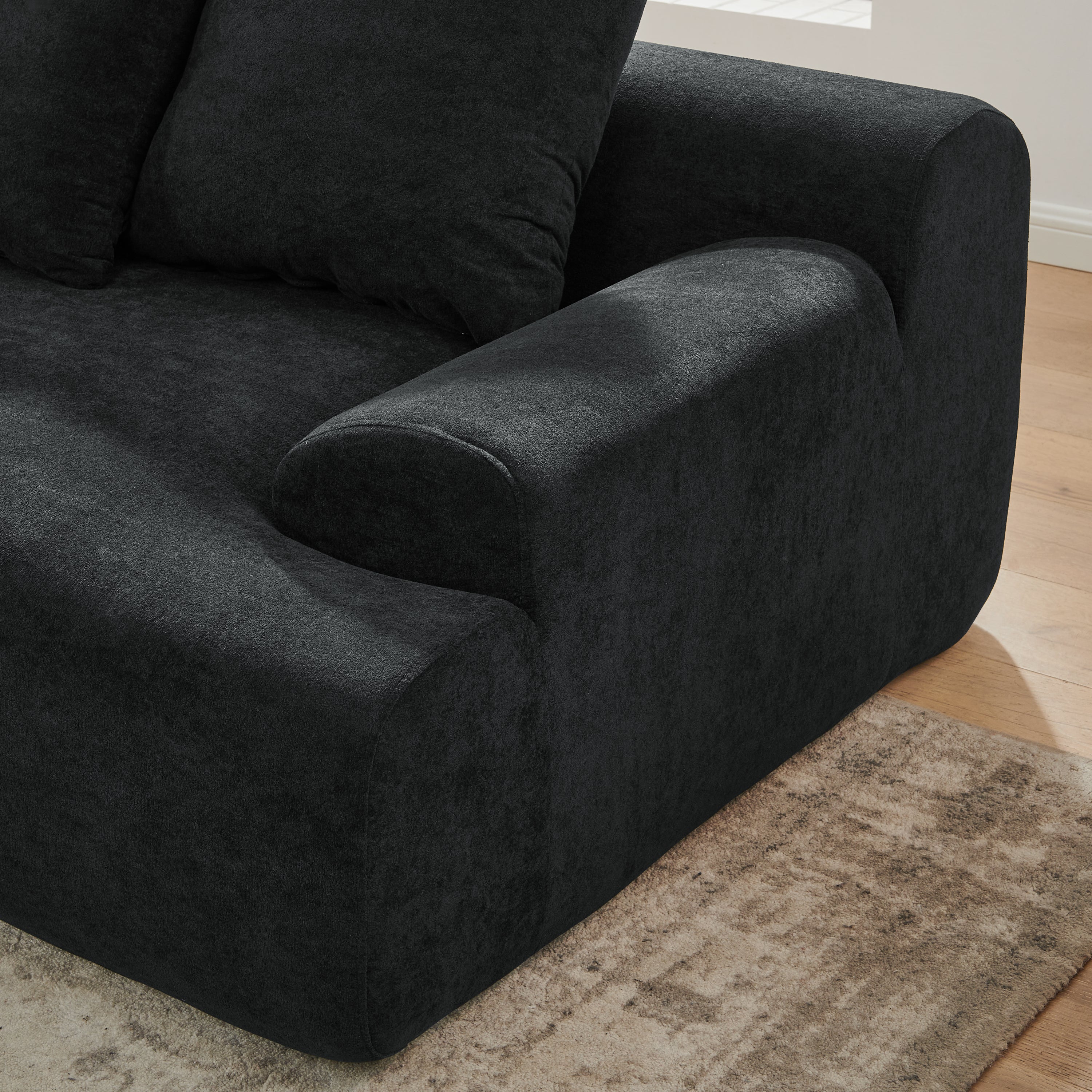 Closeup of contemporary black velvet modular sofa in a living room with large windows and a plant.