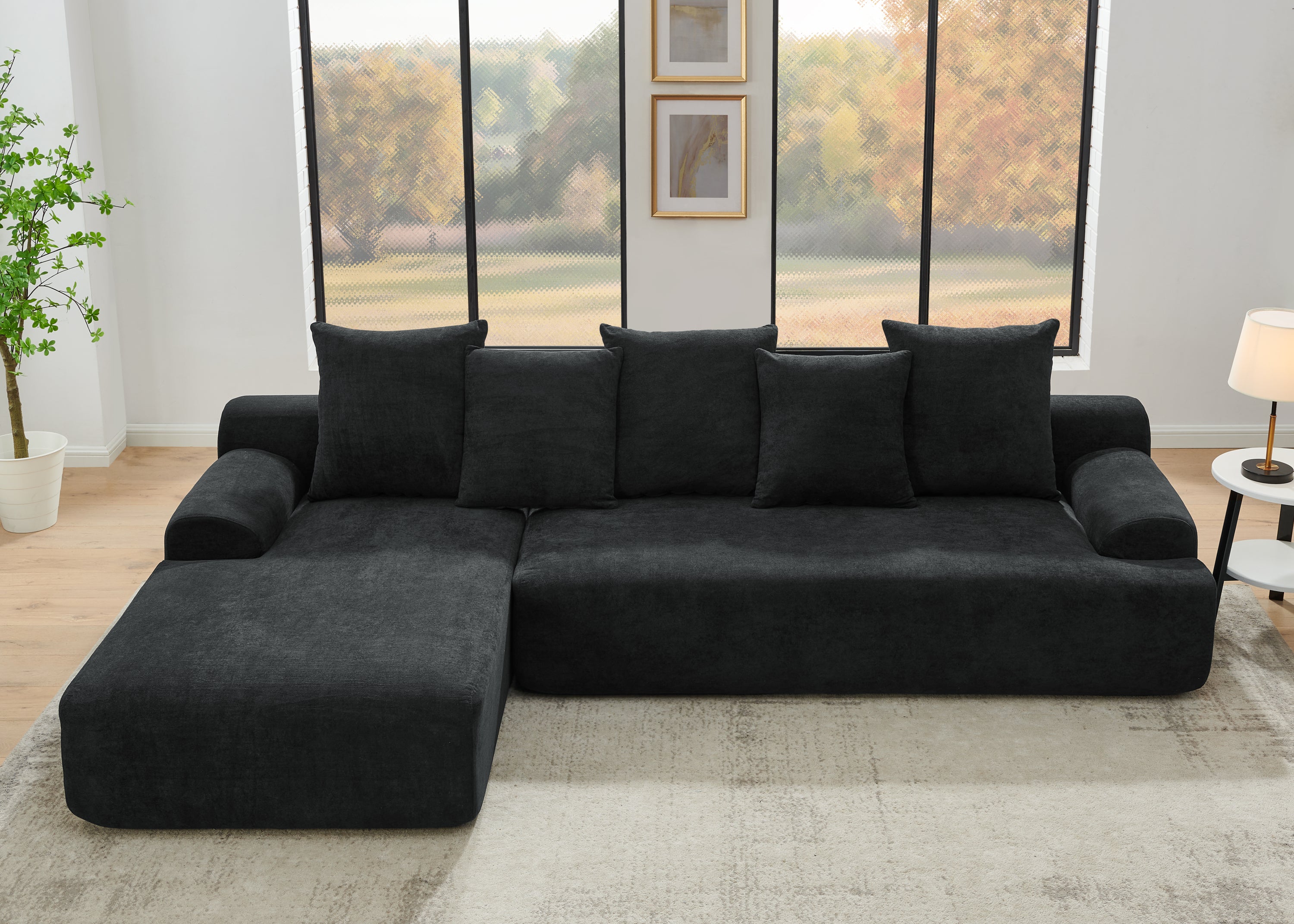 Contemporary black velvet modular sofa in a living room with large windows and a plant.