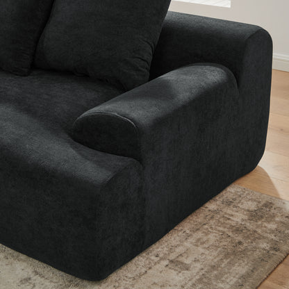 Closeup of contemporary black velvet modular sofa in a living room with large windows and a plant.